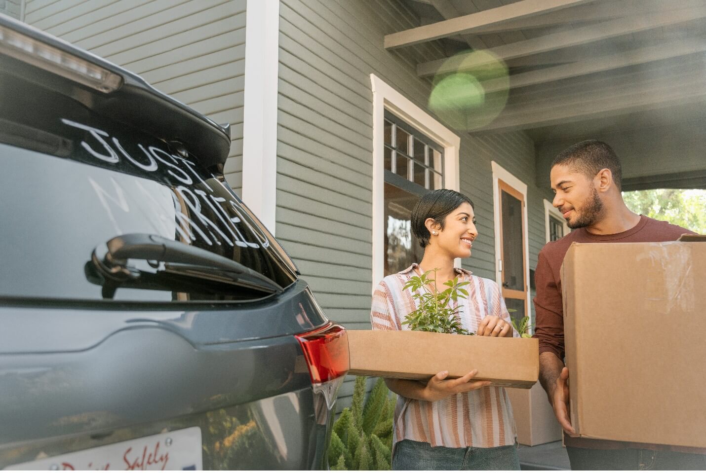 Couple standing behind car holding boxes